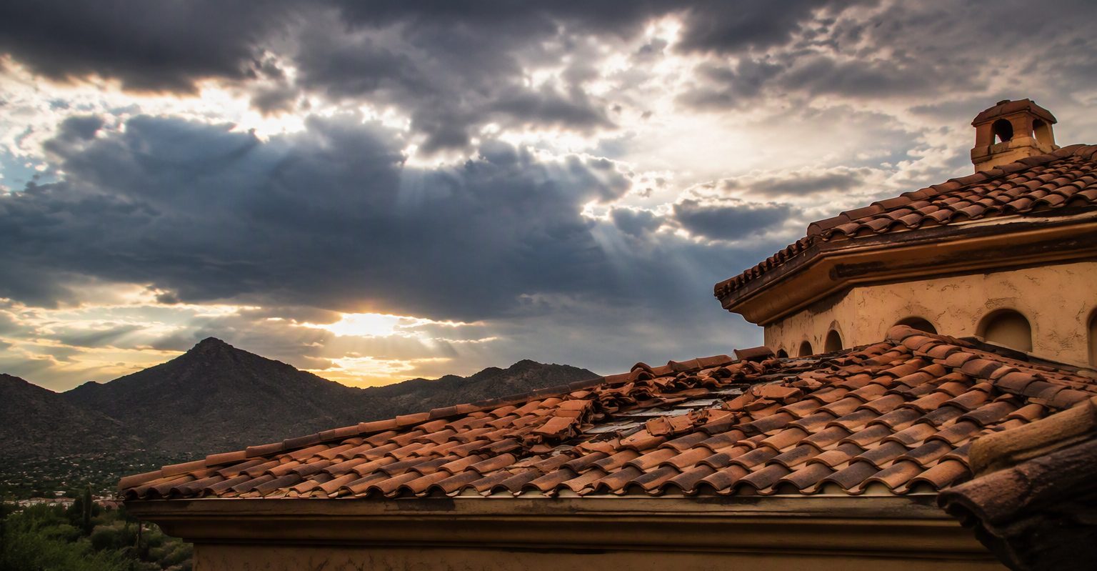 Terracotta barrel-tile roof with displaced tiles under a clearing storm sky, wet tiles glistening
